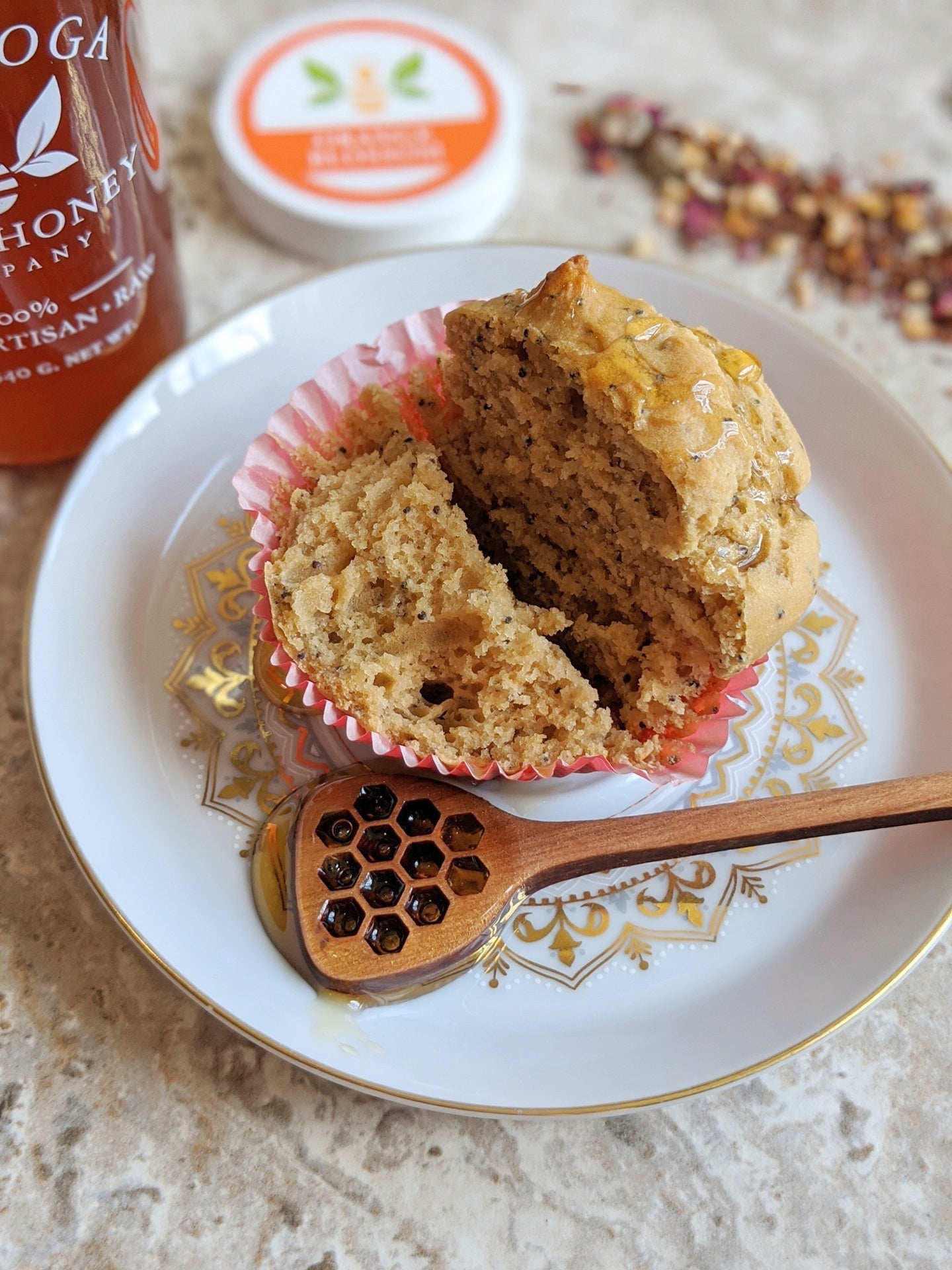 Muffin cut in half on a small plate with a wooden honey dipper in a pool of honey