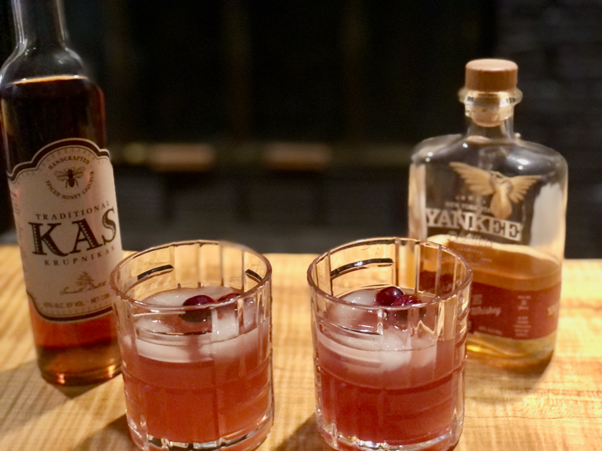 red-hued immune boosting cocktail shrub in lowball glasses in front of KAS honey liquor and Yankee Distiller honey whiskey