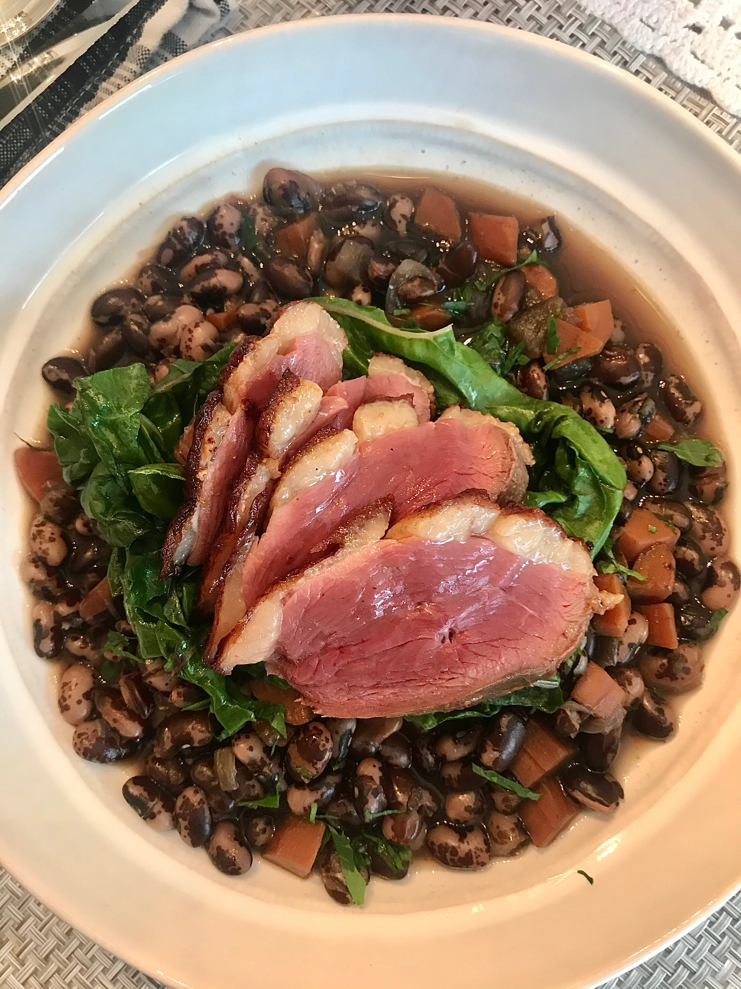 medium rare slices of duck breast laid over greens and calypso beans