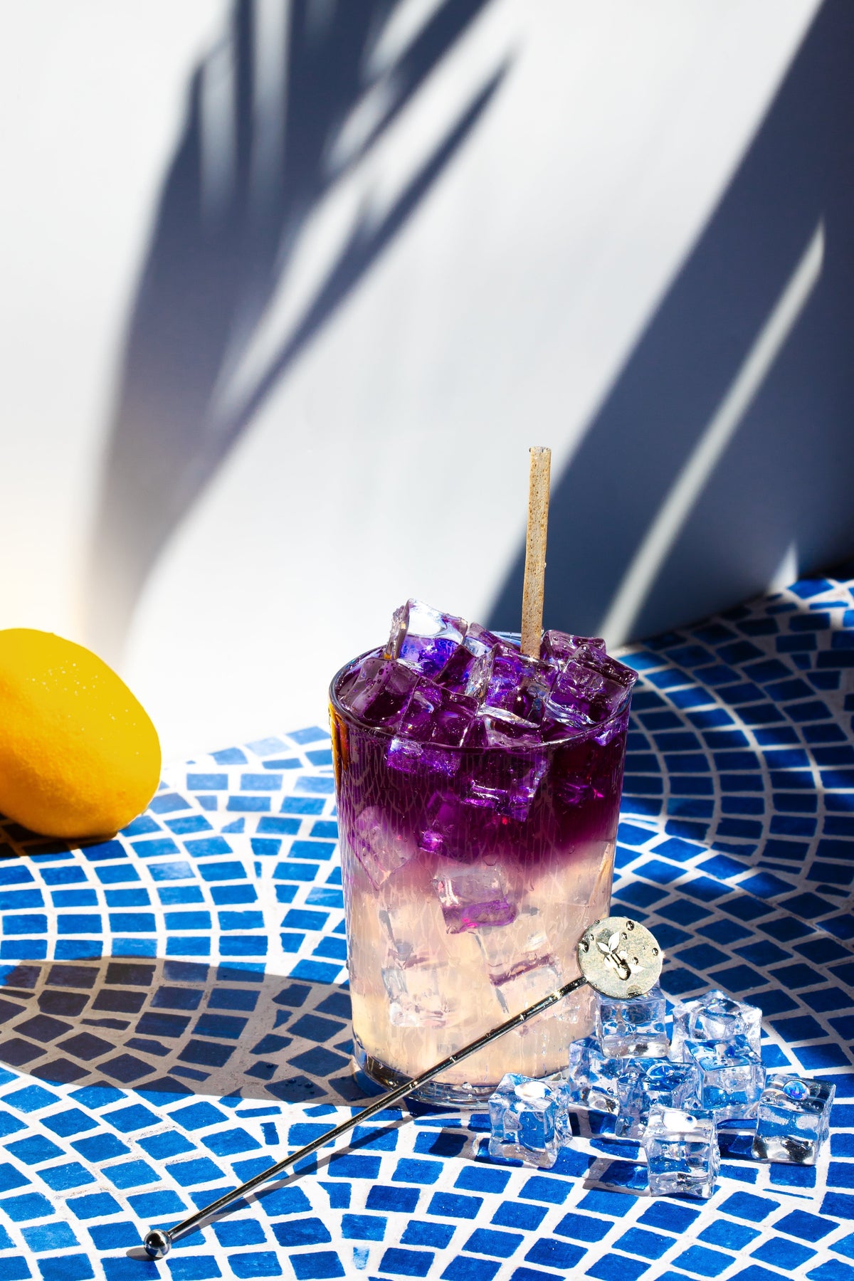 Glass of Lavender Lemonade. Showcases a glass of iced lemonade topped with dark purple iced tea on a blue and white background