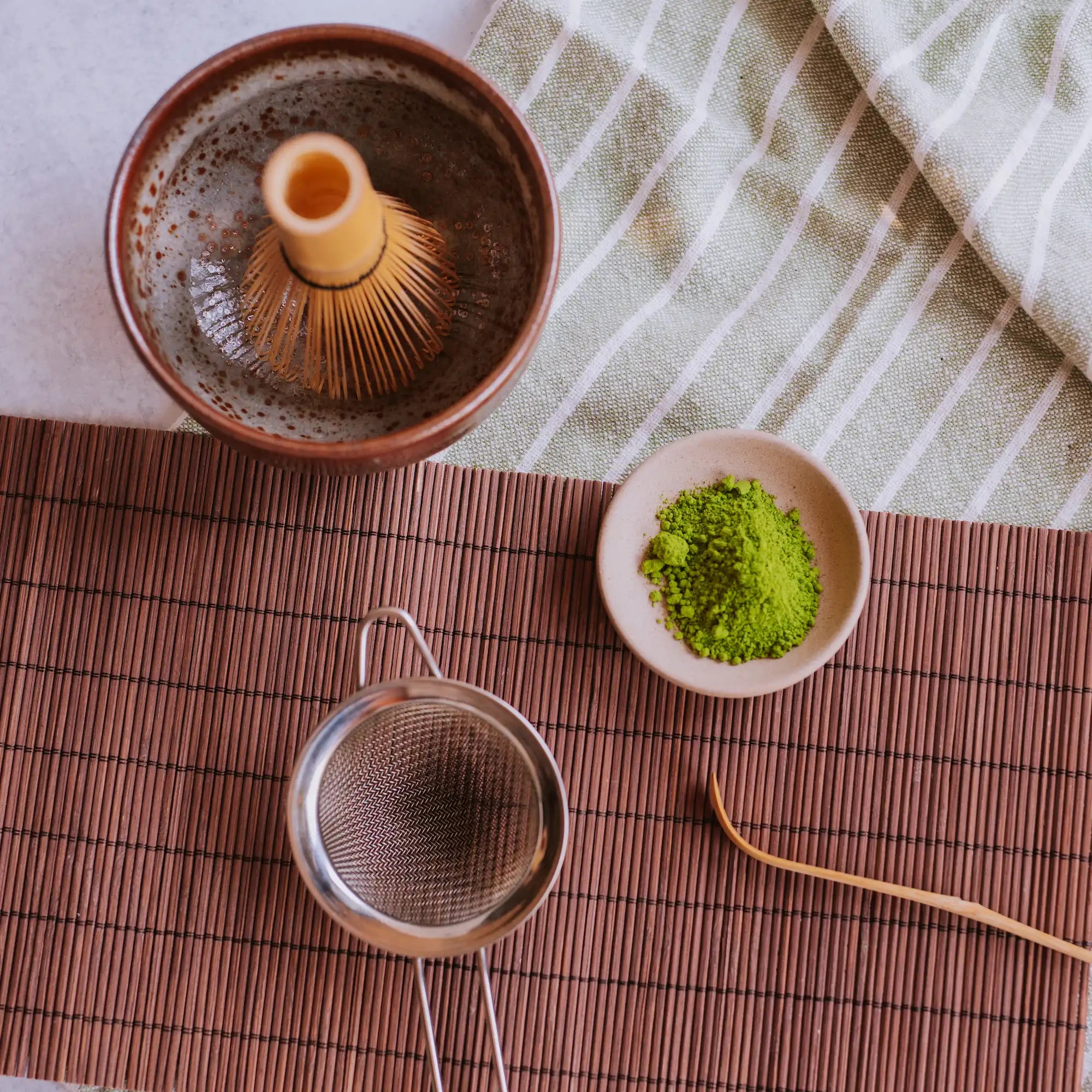 dish of matcha powder with matcha bowl, whisk, sieve, and chashaku