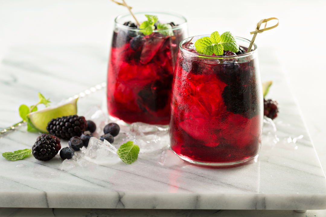 two bright red cocktails garnished with lime and berries on a marble counter