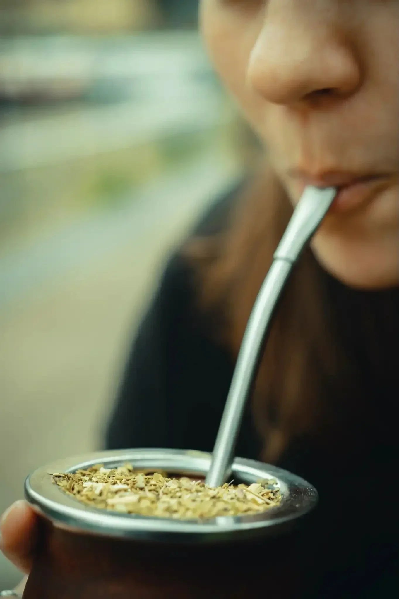 woman drinking yerba mate from a gourd through a metal bombilla (straw)