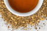 Awakening leaves and brewed tea. Dry, finely chopped mushrooms and herbs surround a cup of honey-brown brewed tea.