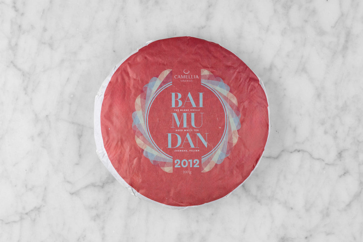 2012 Bai Mu Dan large, round tea cake wrapped in paper with the words "Bai Mu Dan 2012".