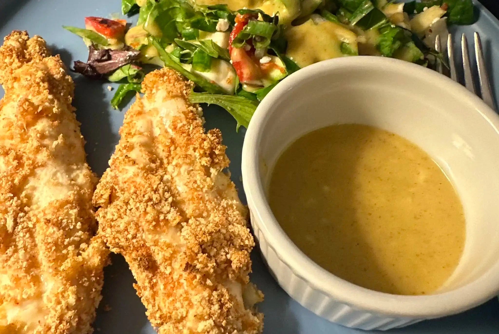 closeup of fried chicken and a salad next to a ramekin of hot honey mustard