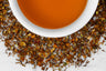 Close up of dry and brewed Island Glow. The dry tea is composed of rooibos with turmeric, mango, and coconut pieces surrounding a cup of brewed, orange-hued tea.