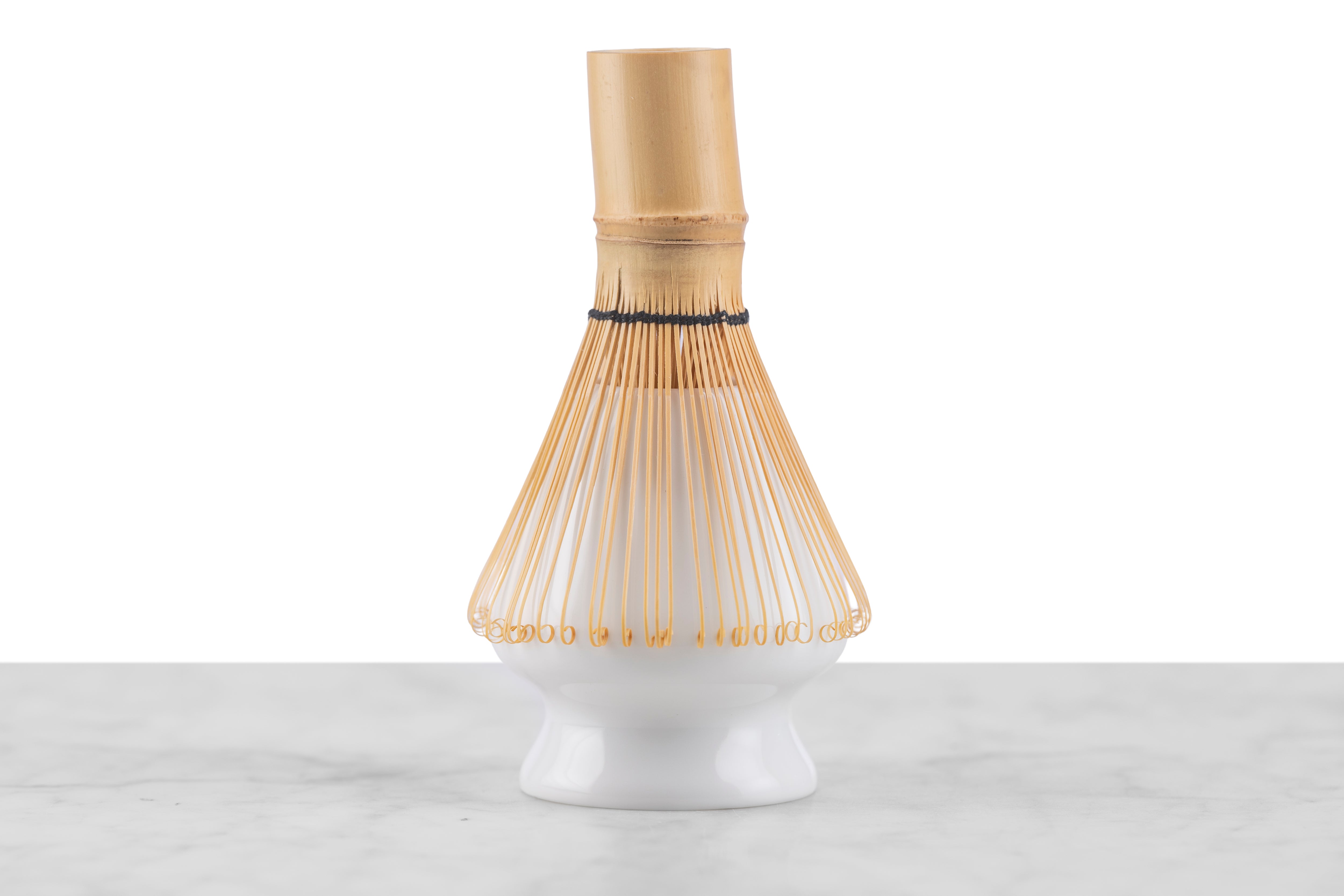 A white ceramic matcha whisk stand with a matcha whisk resting on it.
