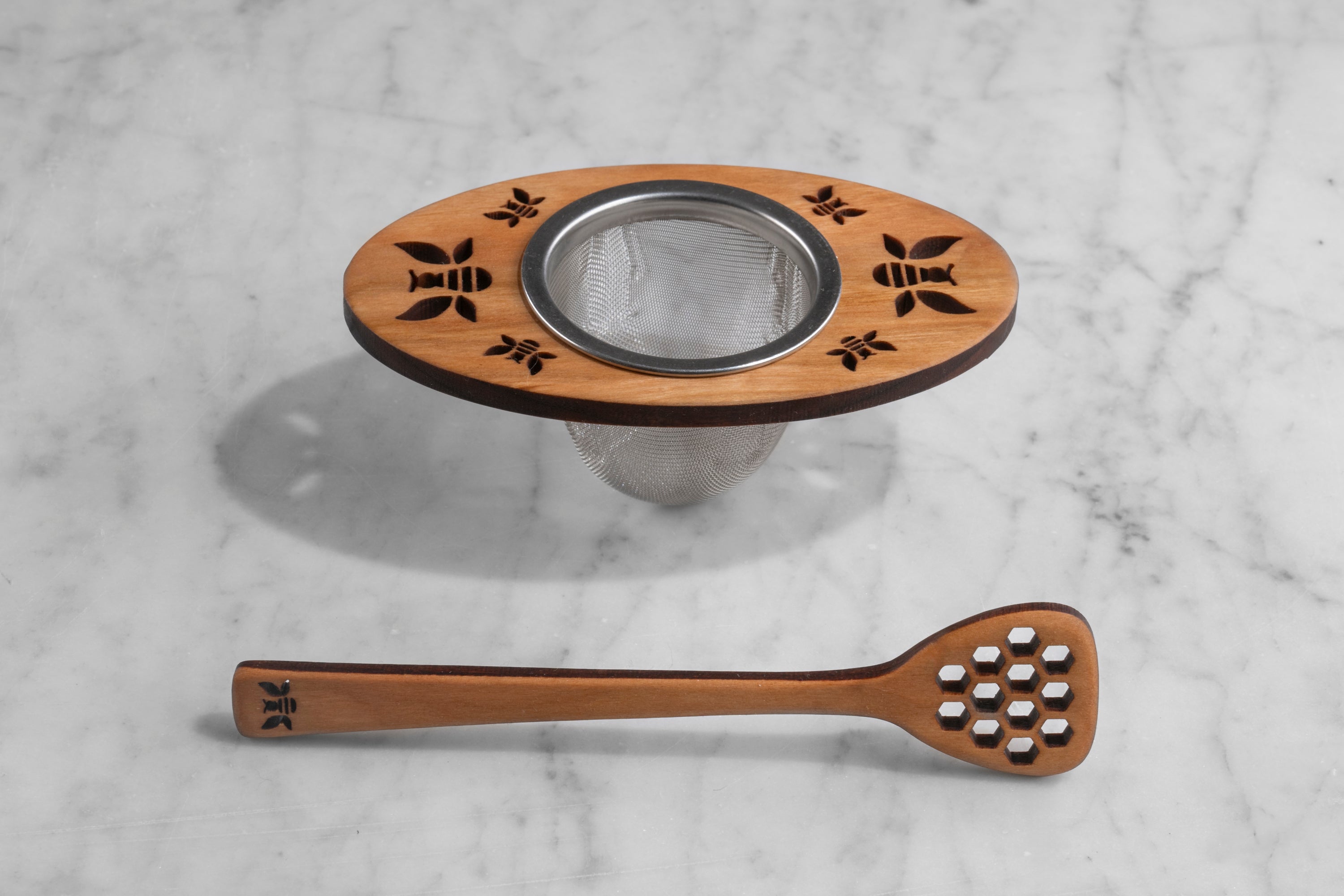 wooden and metal tea infuser and honey dipper with bee motif on marble background
