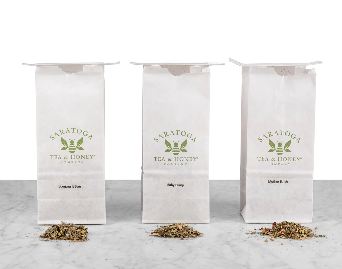 The three Motherhood & Fertility Bundle Teas lined up next to each other in white Saratoga Tea & Honey Co. tea bags with piles of corresponding teas in front: Bonjour Bebe, Baby Bump & Mother Earth