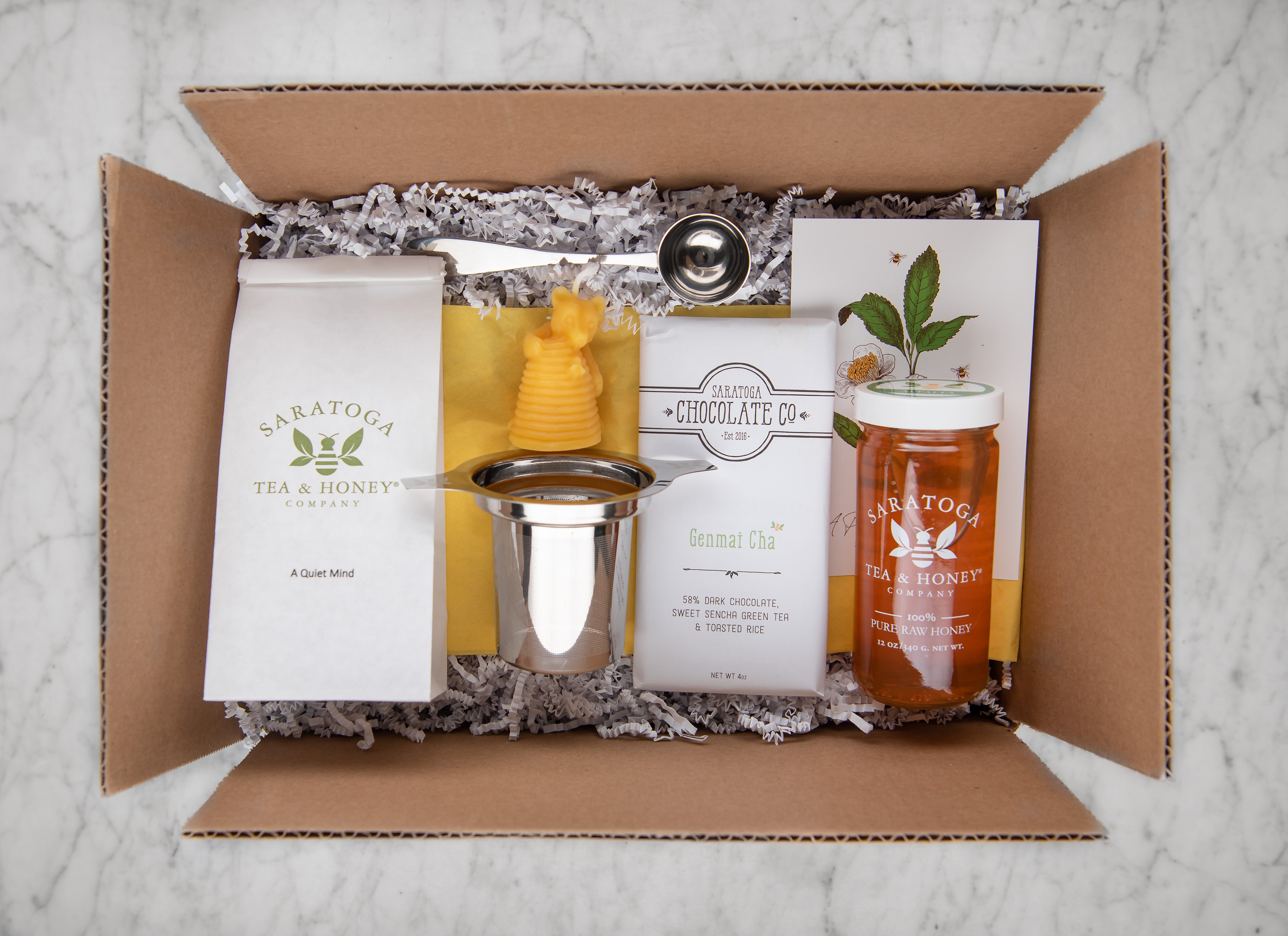 new baby tea and honey gift set featuring a quiet mind calming tea, alfalfa honey, a tea infuser, tea scoop, bear beeswax candle, and dark chocolate bar