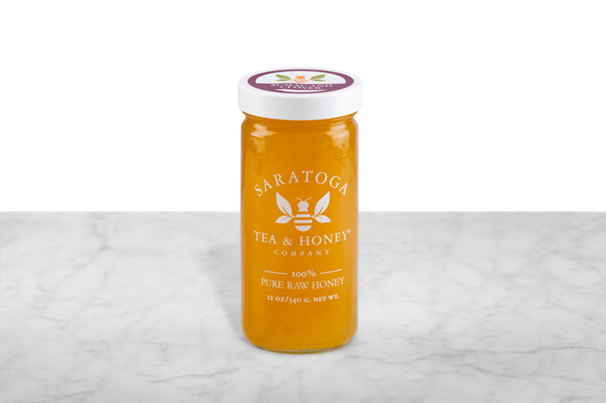 Opaque, amber-hued Sumac & Clover Honey displayed in a 12oz cylindrical glass jar with a white lid. The logo and the words: "100% Pure Raw Honey" are printed on the jar.