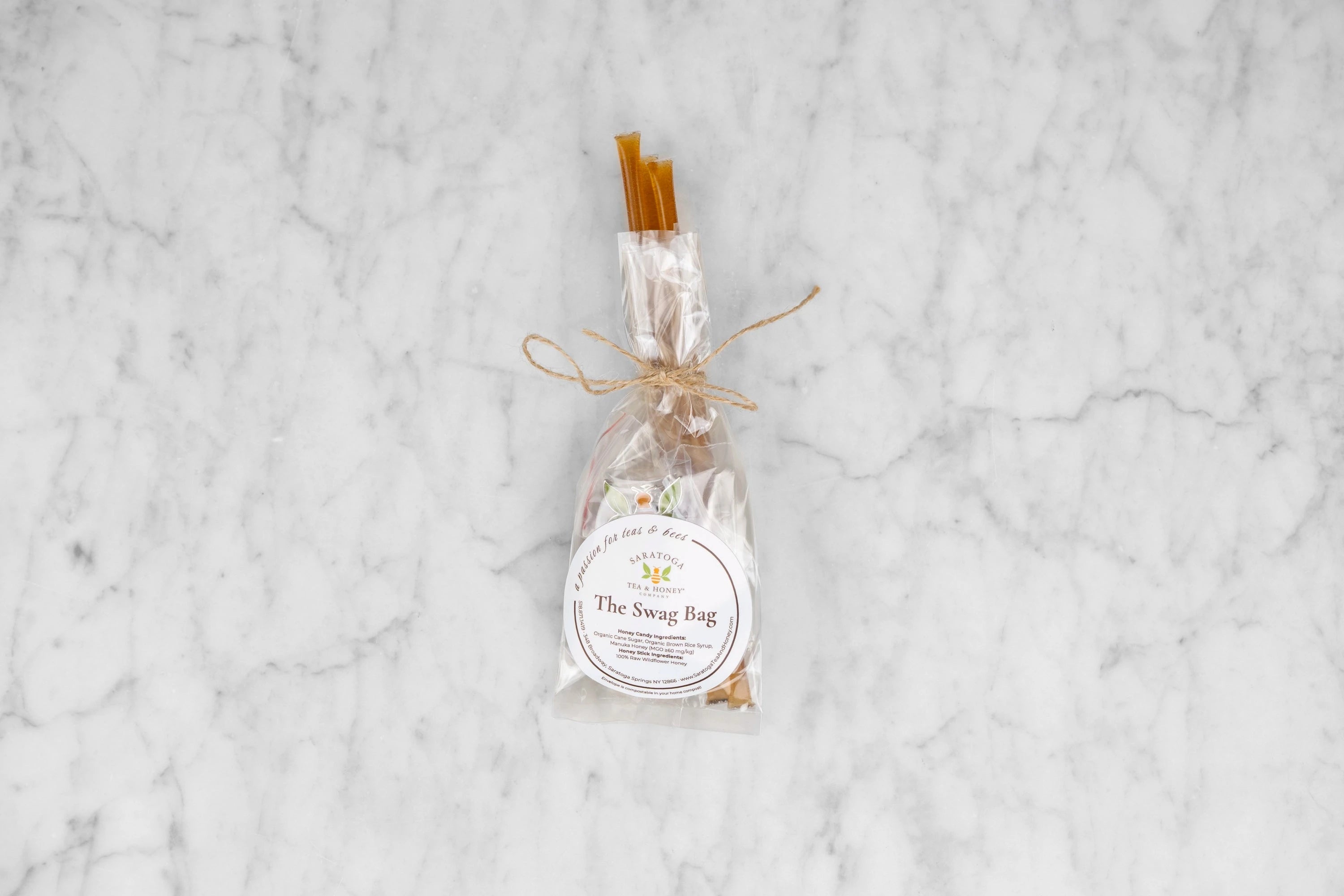 The Swag Bag example product. Three honey sticks, three round hard honey candies, a Saratoga Tea & Honey Co. sticker and a tea bee enamel pin in a clear, compostable bag tied with twine.