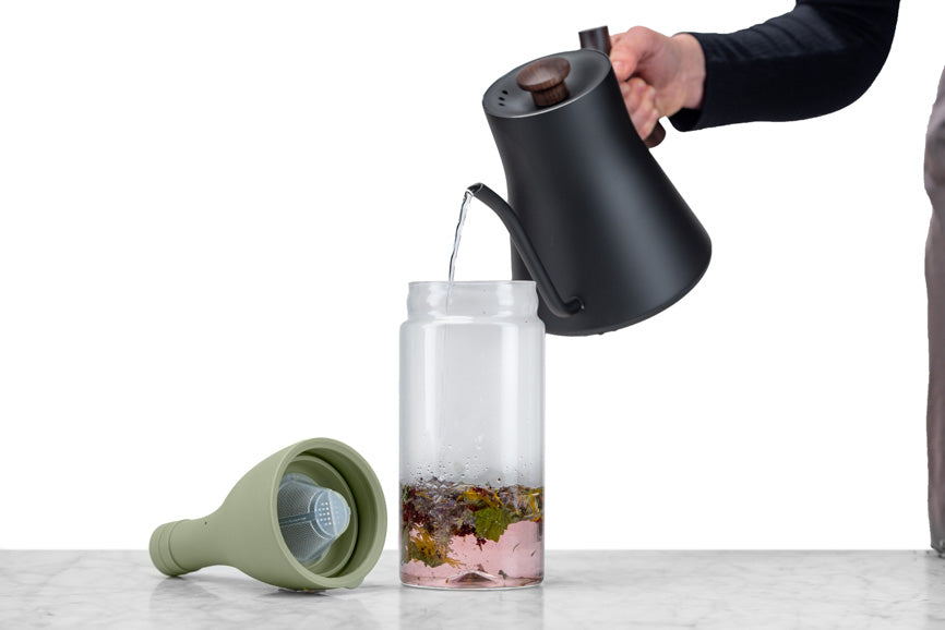 hand poruing water from teapot into an iced tea bottle