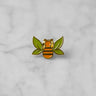 "Tea Bee" gold enamel pin with green tea leaf wings and orange bee body centered on marble. 