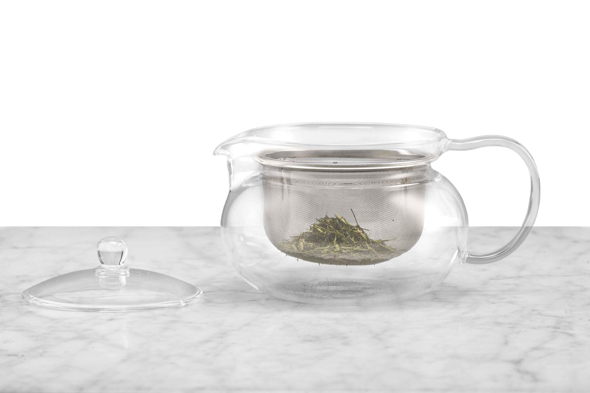 A glass teapot with a metal infuser holding dry tea leaves.