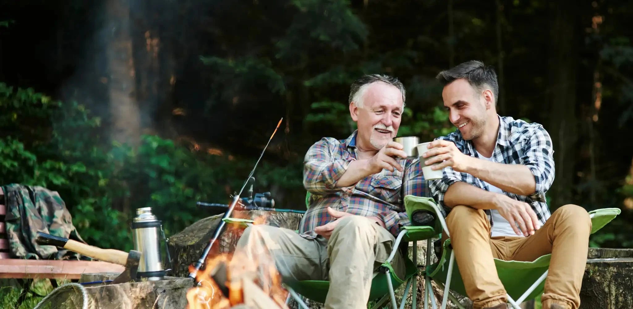 father and son toasting hot beverages in front of a campfire