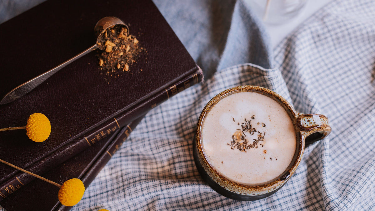 cozy chai tea latte next to stack of books and loose leaf chai spilling from a tea scoop