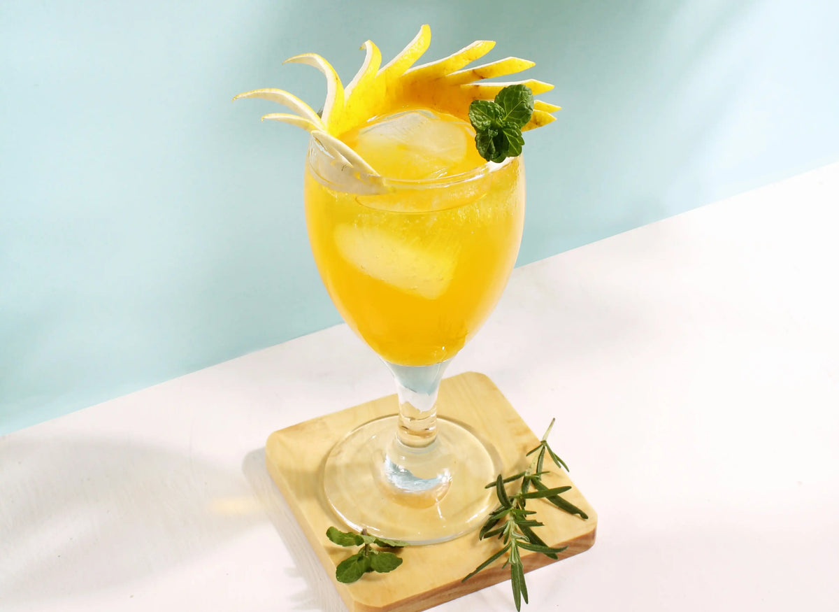 glass of an orange colored cocktail garnished with a fringed orange slice and sprig of mint