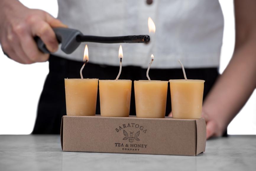 woman lighting beeswax votive candles sitting on a kraft box