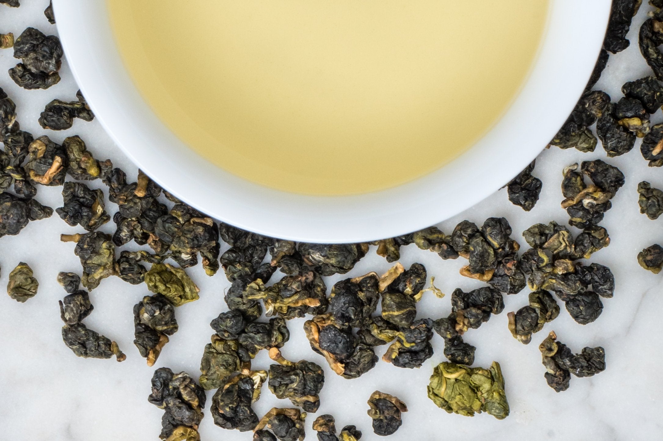 loose leaf rolled Taiwanese Ali Shan oolong surrounding a white cup with brewed tea