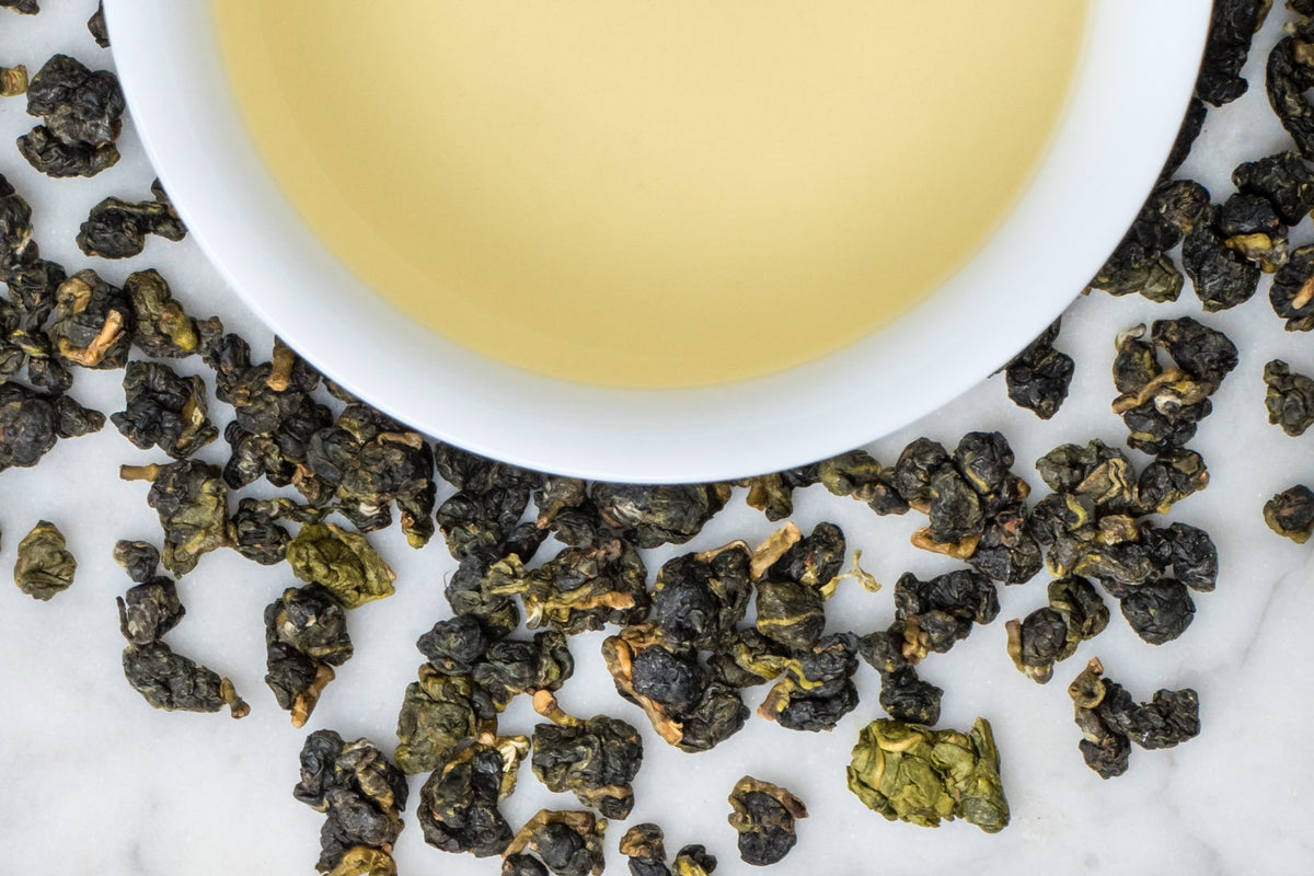 loose leaf rolled Taiwanese Ali Shan oolong surrounding a white cup with brewed tea