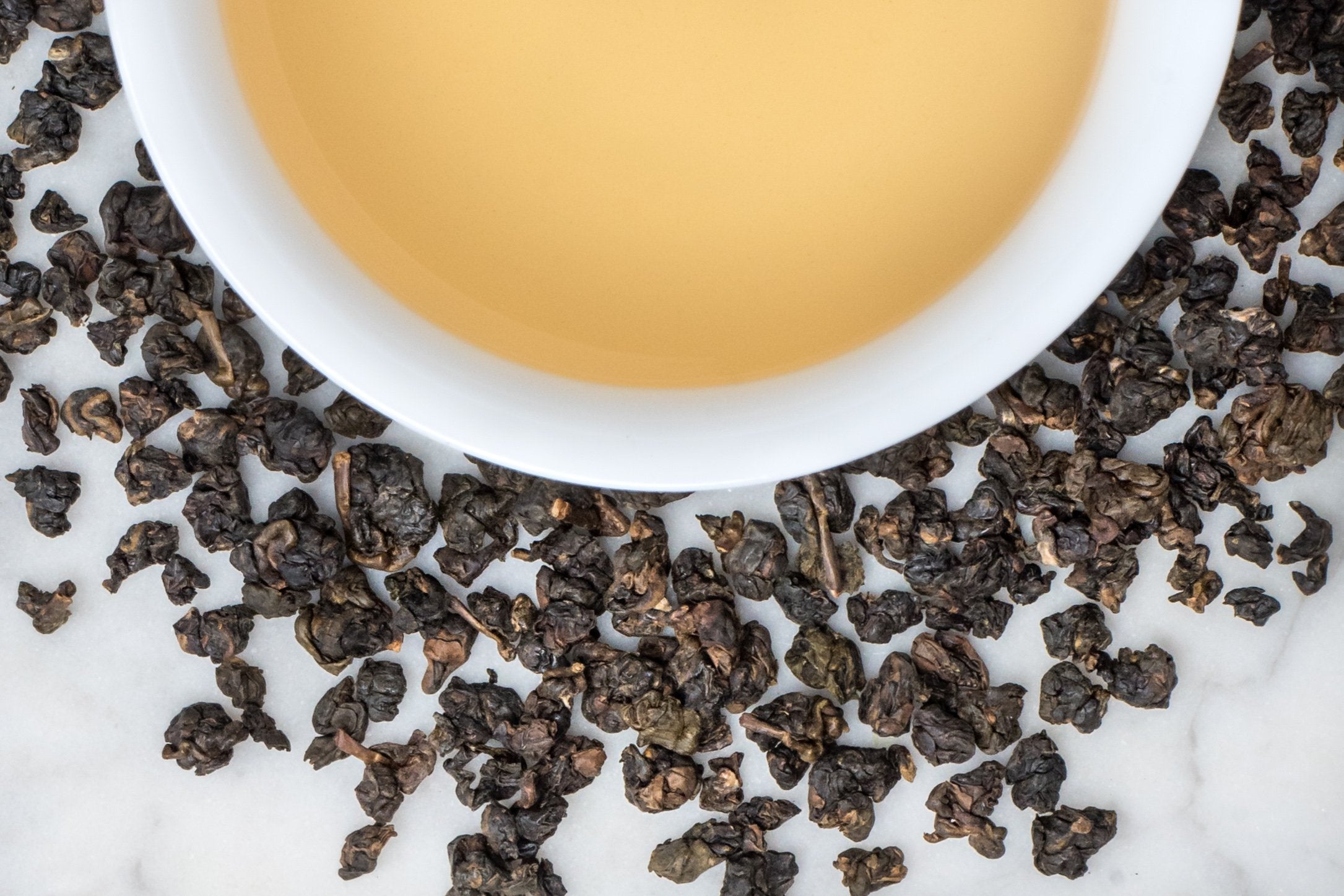 Dong Ding - Roasted, leaves and brewed tea. Small, tightly furled balls of dark brownish green oolong surround a cup of pale-gold colored brewed tea. 