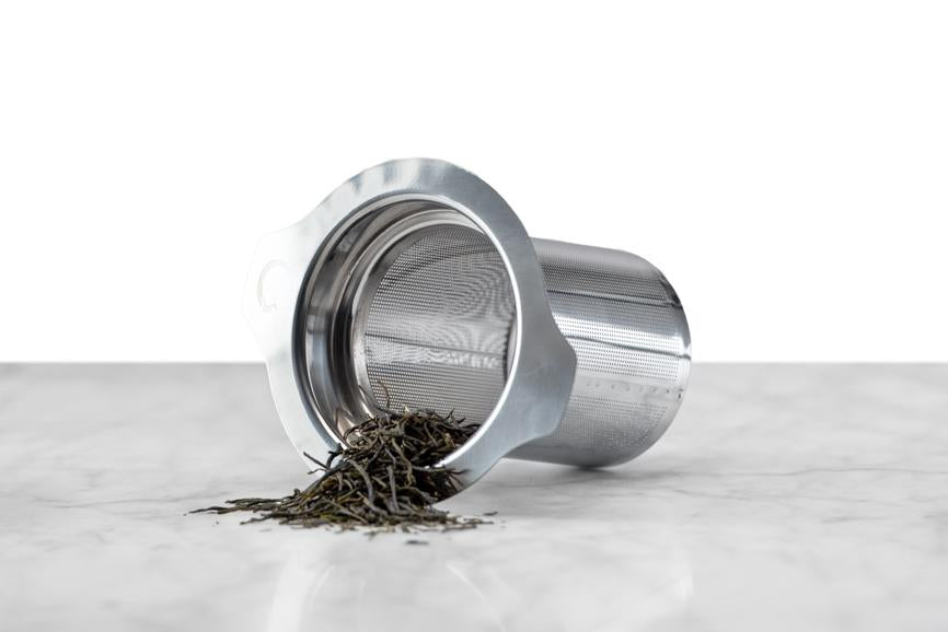 tea spilling out of a stainless steel tea infuser on a marble and white background
