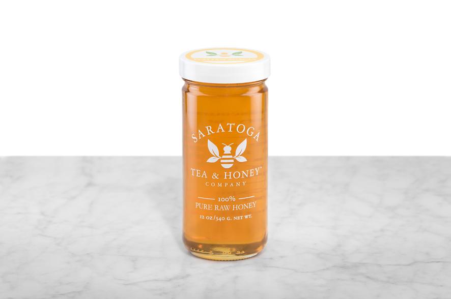 Golden Acacia Honey displayed in a 12oz cylindrical glass jar with a white lid. The logo and the words: "100% Pure Raw Honey" are printed on the jar.