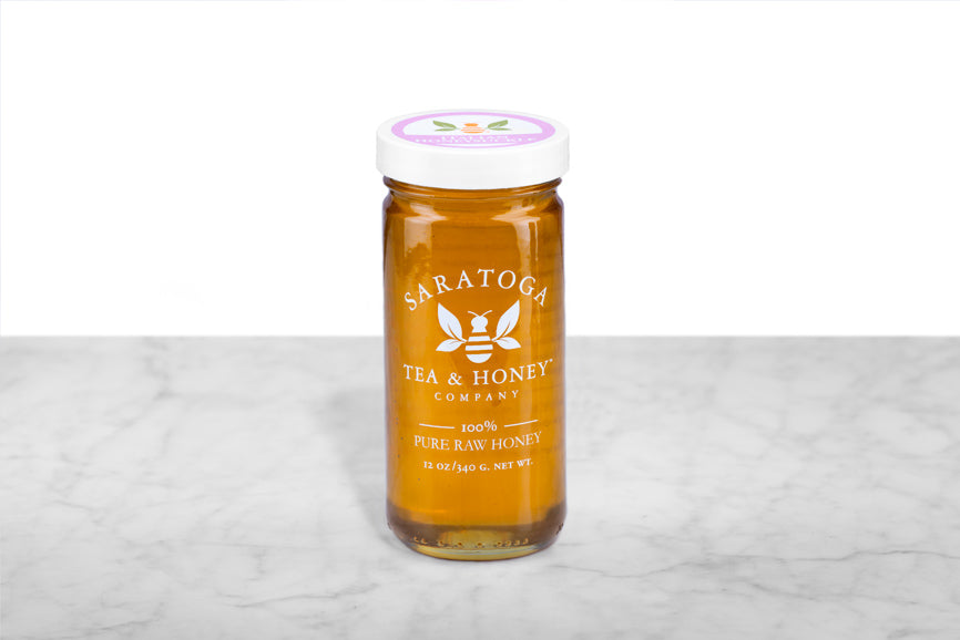 Golden Italian Honeysuckle Honey displayed in a 12oz cylindrical glass jar with a white lid. The logo and the words: "100% Pure Raw Honey" are printed on the jar.