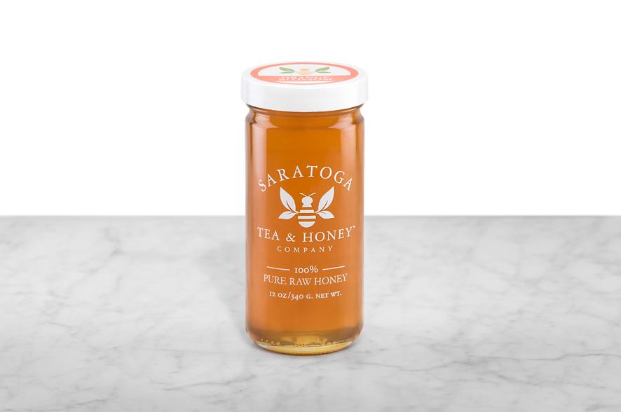 Amber-hued Orange Blossom Honey displayed in a 12oz cylindrical glass jar with a white lid. The logo and the words: "100% Pure Raw Honey" are printed on the jar.