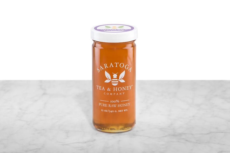 Amber-hued Spanish Wild Lavender Honey displayed in a 12oz cylindrical glass jar with a white lid. The logo and the words: "100% Pure Raw Honey" are printed on the jar.