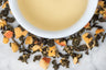 The Apricot Queen leaves and brewed tea. Rolled oolong and dried apricot bits surround a cup of pale yellow brewed tea.