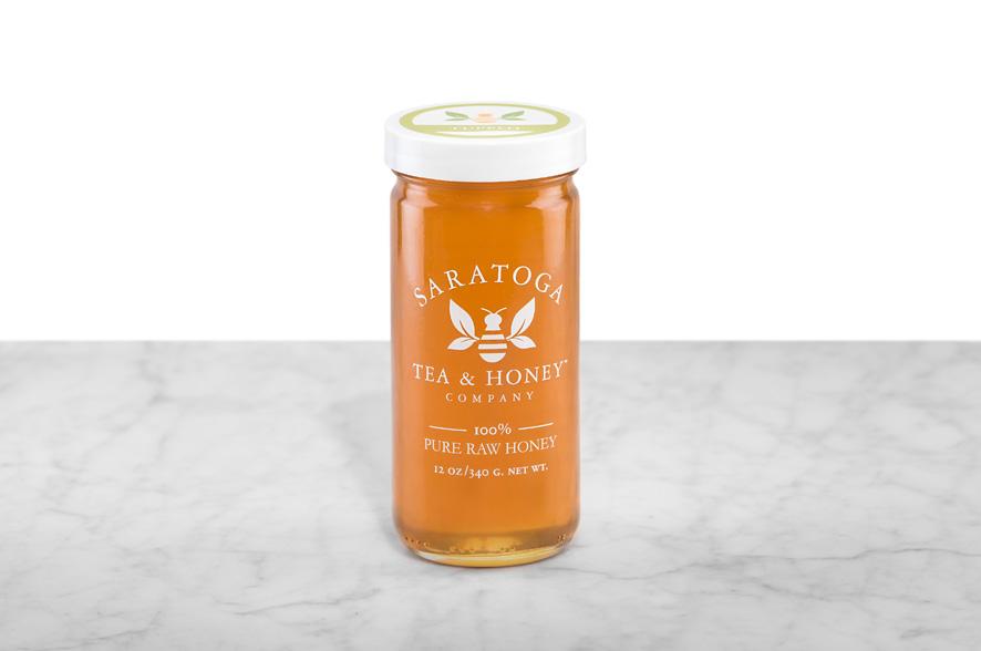Golden-amber Tupelo Honey displayed in a 12oz cylindrical glass jar with a white lid. The logo and the words: "100% Pure Raw Honey" are printed on the jar.
